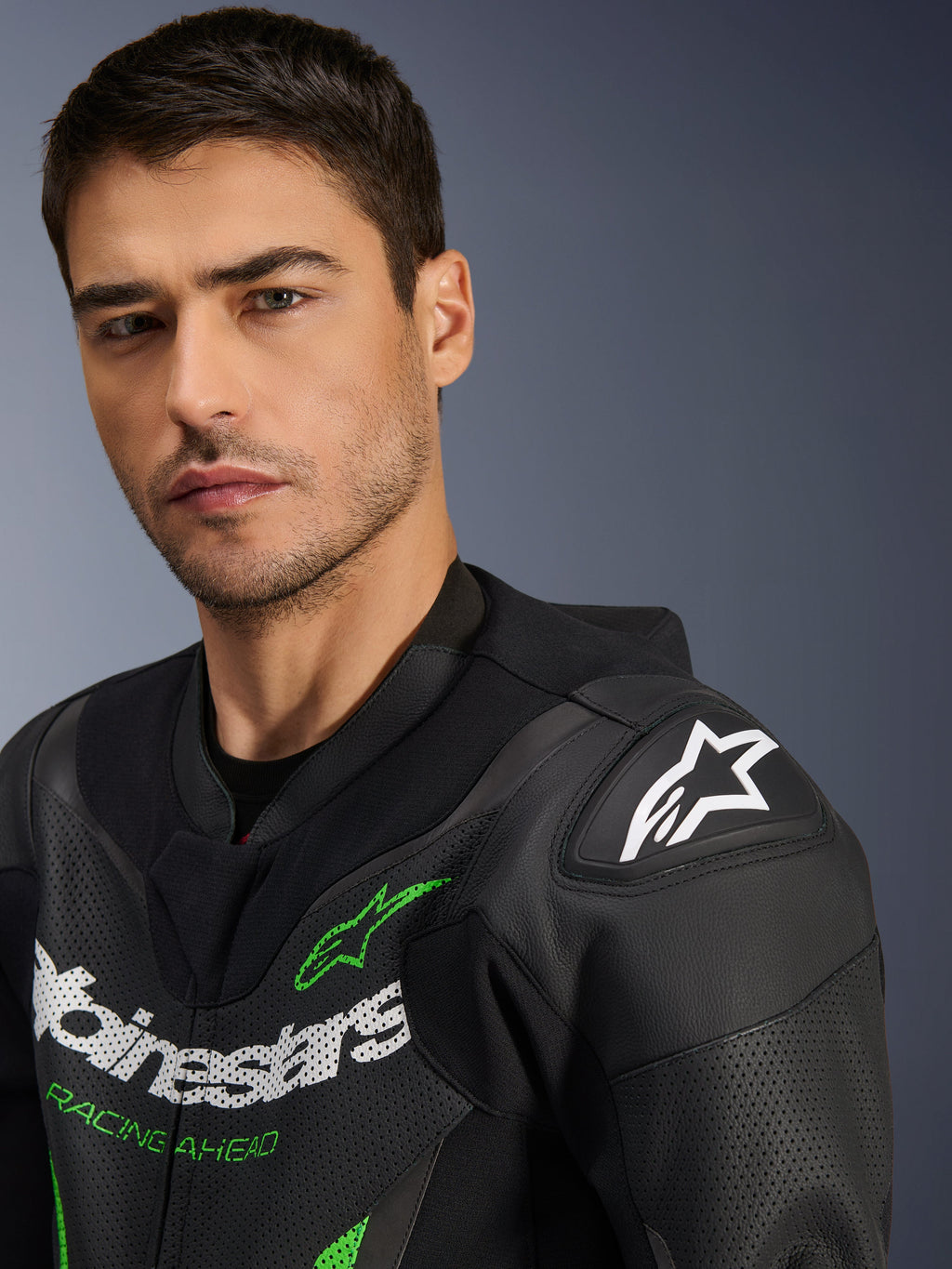 Alpinestars GP Force V2 Leren Pak - 1-delig, zwart en groen, close-up van een mannelijk model dat het motorpak draagt, met witte en groene logo's, geperforeerde leren panelen en DFS Lite schouderbescherming met een wit sterlogo.