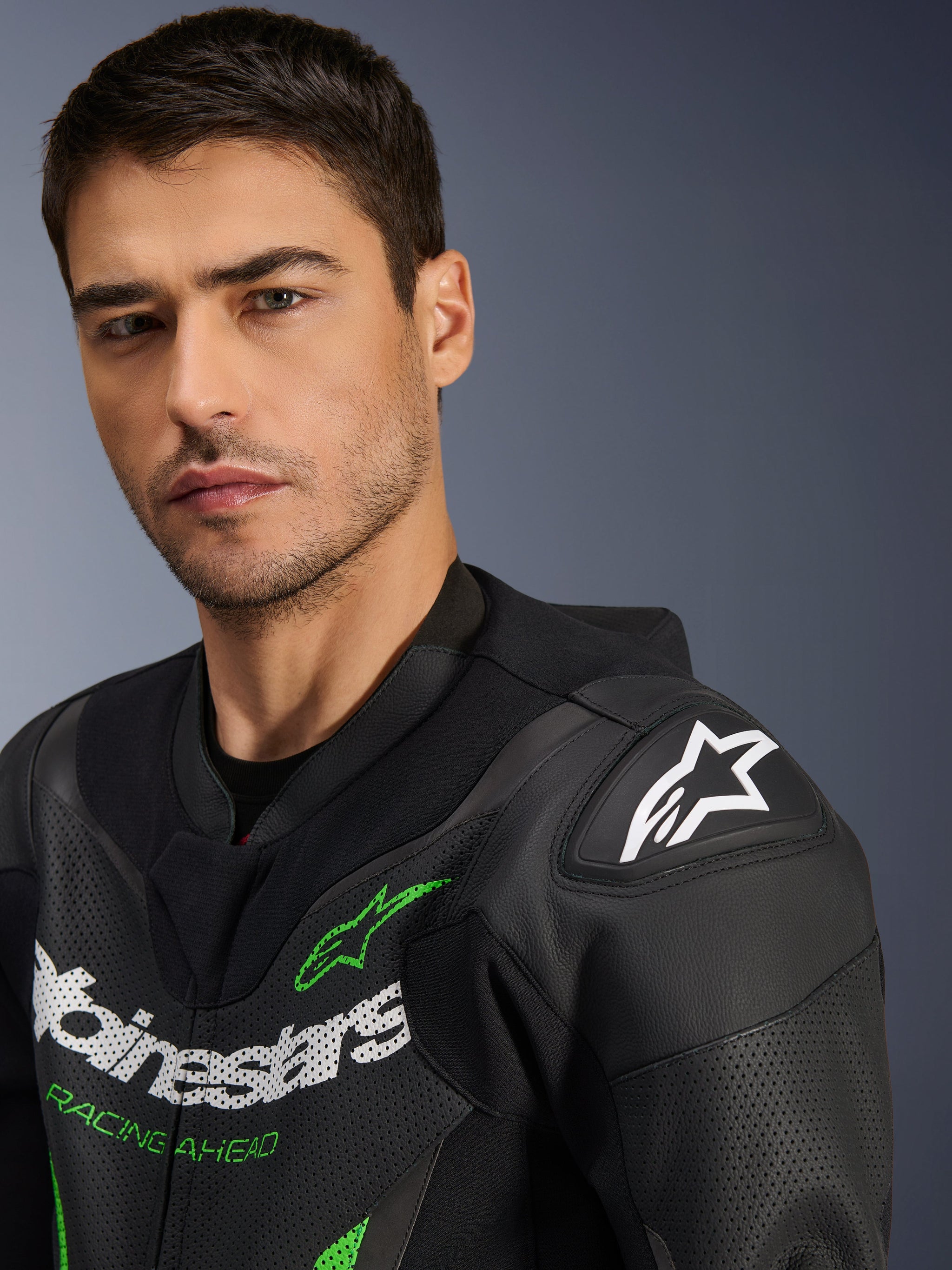 Alpinestars GP Force V2 Leren Pak - 1-delig, zwart en groen, close-up van een mannelijk model dat het motorpak draagt, met witte en groene logo's, geperforeerde leren panelen en DFS Lite schouderbescherming met een wit sterlogo.