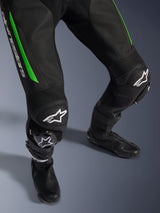 Alpinestars GP Force V2 Leren Pak - 1-delig, close-up van de benen in zwart en groen, voorzien van geperforeerde leren constructie, accordeon stretchpanelen bij de knieën, witte Alpinestars logo's en geïntegreerde kniesliders, gedragen met zwarte racelaarzen