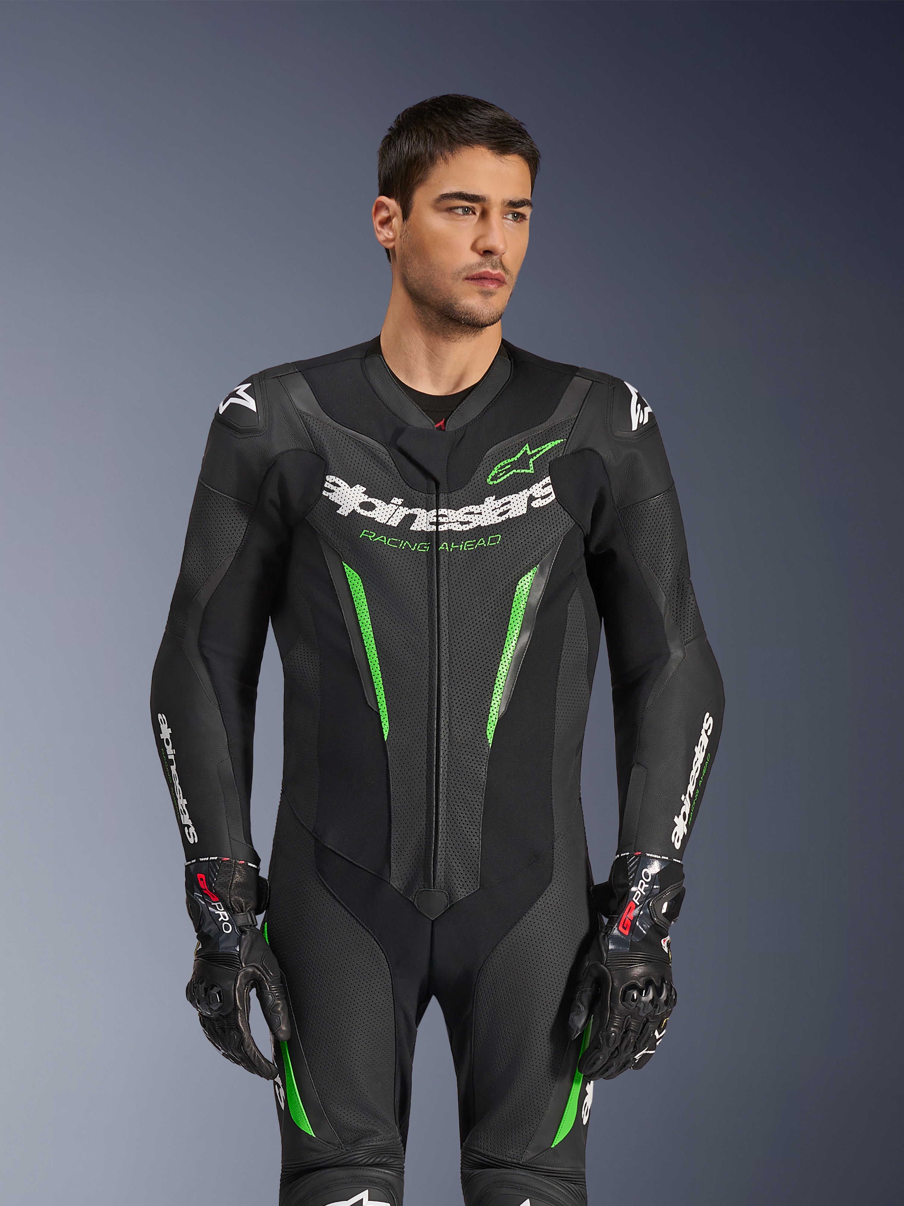 Alpinestars GP Force V2 Leren Pak - 1-delig, zwart en groen motorracepak, gedragen door een model, met geperforeerde leren panelen, opvallende witte Alpinestars-branding op de borst en mouwen en geïntegreerde schouderbescherming voor circuitprestaties.