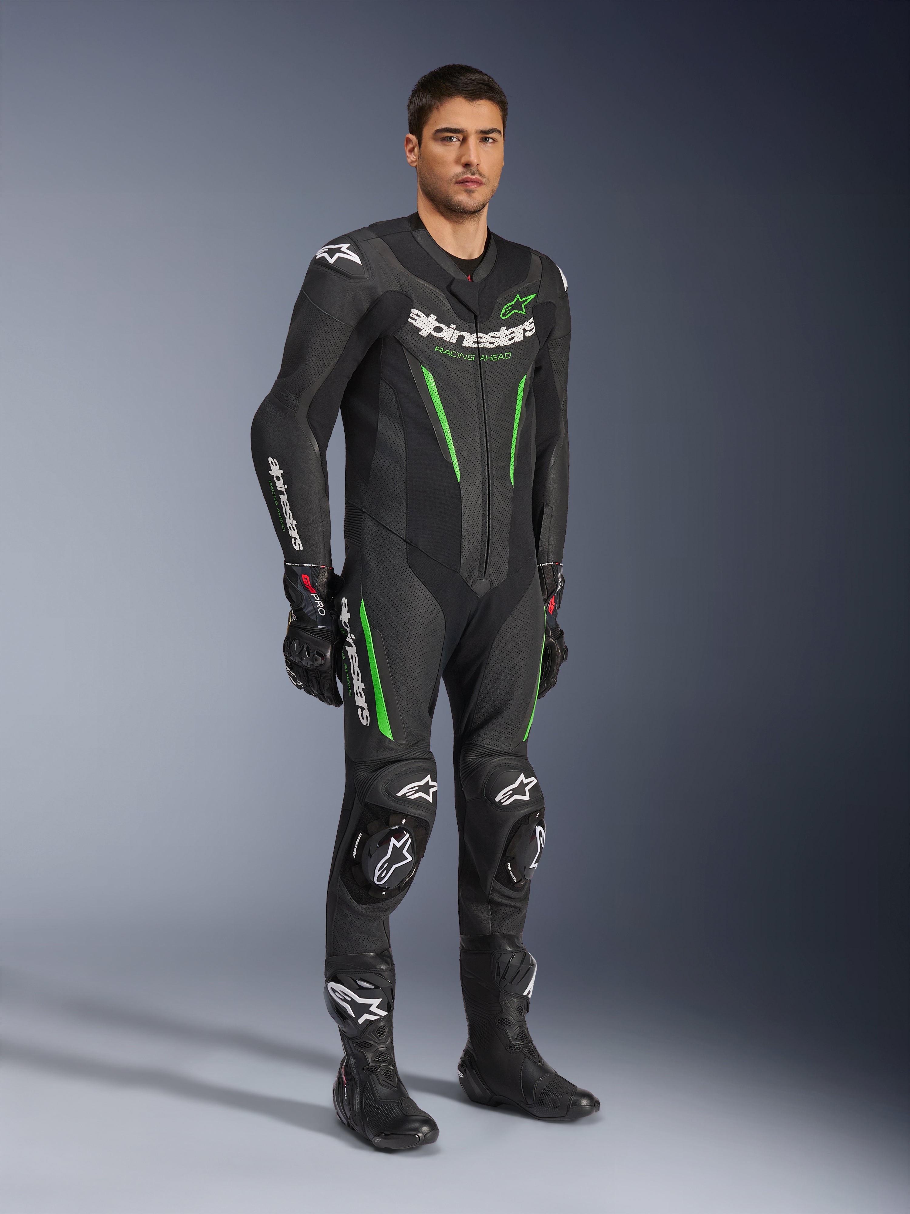 Alpinestars GP Force V2 Leren Pak 1-delig, zwart en groen, volledige race-uitrusting gedragen met zwarte handschoenen en laarzen, voorzien van geperforeerde leren panelen, witte Alpinestars-branding en geïntegreerde kniesliders, professioneel racepak voor circuitprestaties