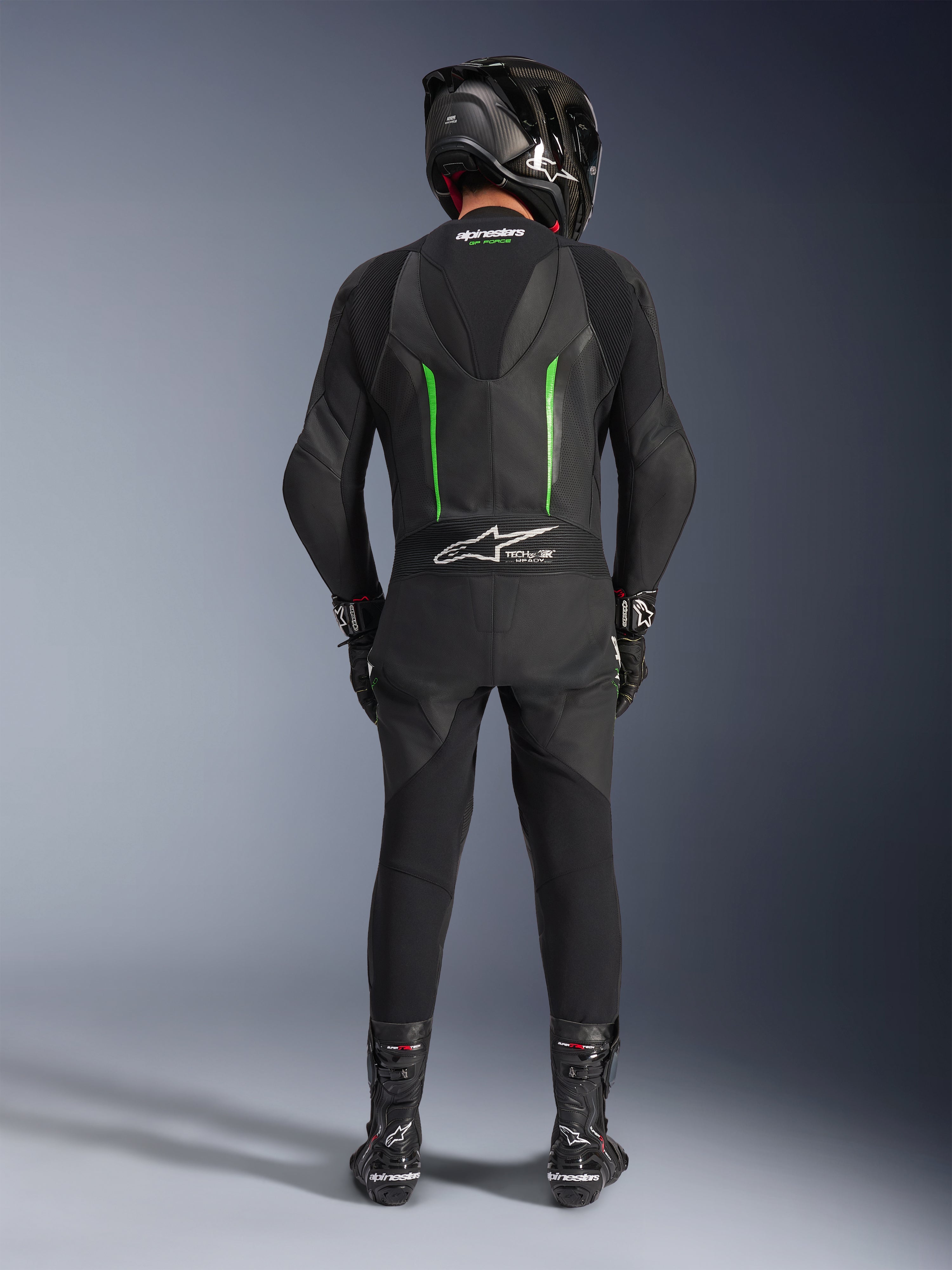 Rijder van achteren in het Alpinestars GP Force V2 Leren Pak - 1-delig in zwart en groen, gecombineerd met een zwarte carbon helm, zwarte racehandschoenen en zwarte laarzen, voorzien van een aerodynamische speed hump en Tech-Air Ready branding.
