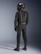 Rijder van achteren gezien in Alpinestars GP Force V2 Leren Pak, 1-delig, zwart met groene accenten, aerodynamische speed hump, gecombineerd met een zwarte carbon helm, zwarte racelaarzen en handschoenen, hoogwaardige motorrace-uitrusting