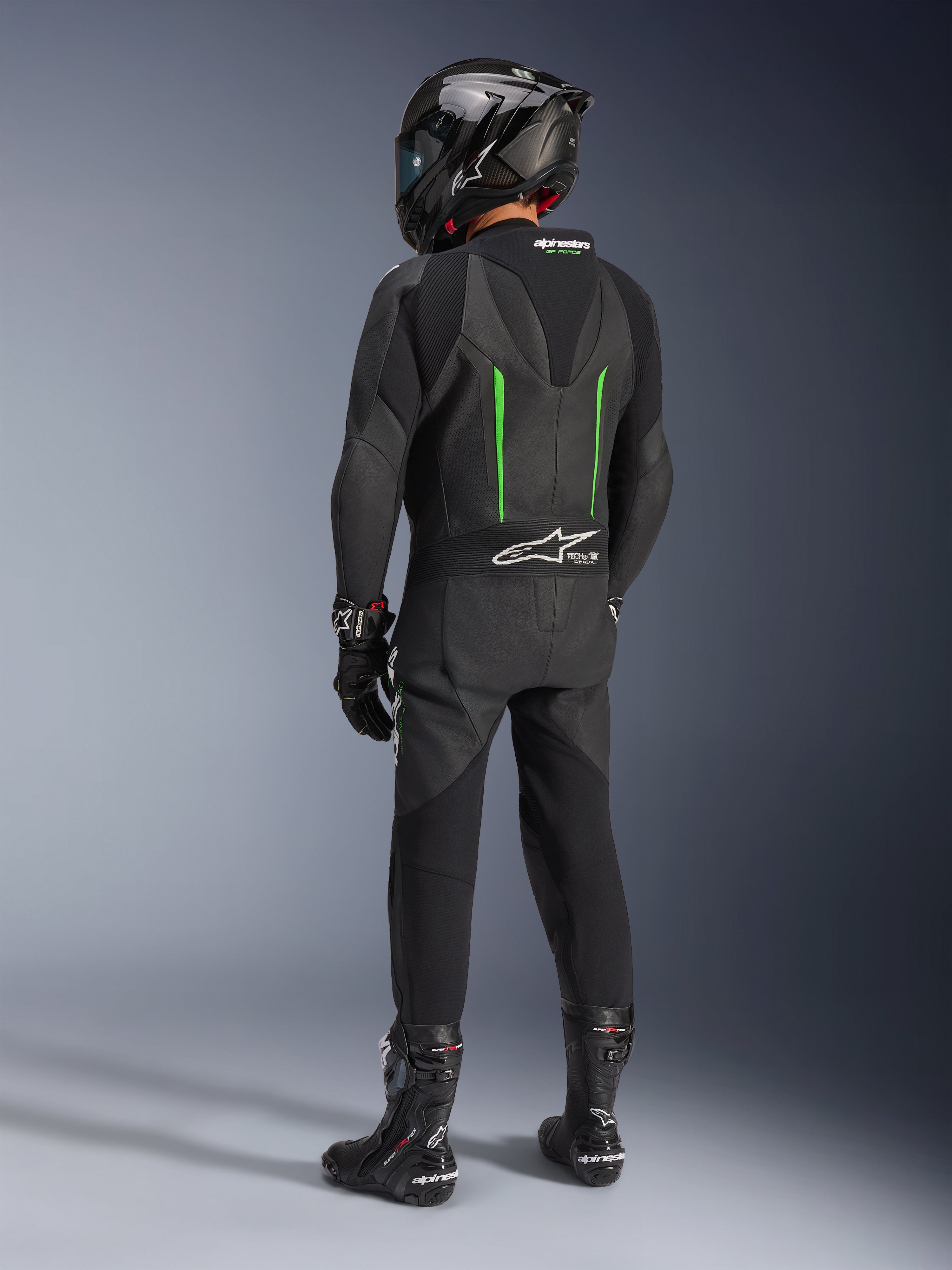 Rijder van achteren gezien in Alpinestars GP Force V2 Leren Pak, 1-delig, zwart met groene accenten, aerodynamische speed hump, gecombineerd met een zwarte carbon helm, zwarte racelaarzen en handschoenen, hoogwaardige motorrace-uitrusting