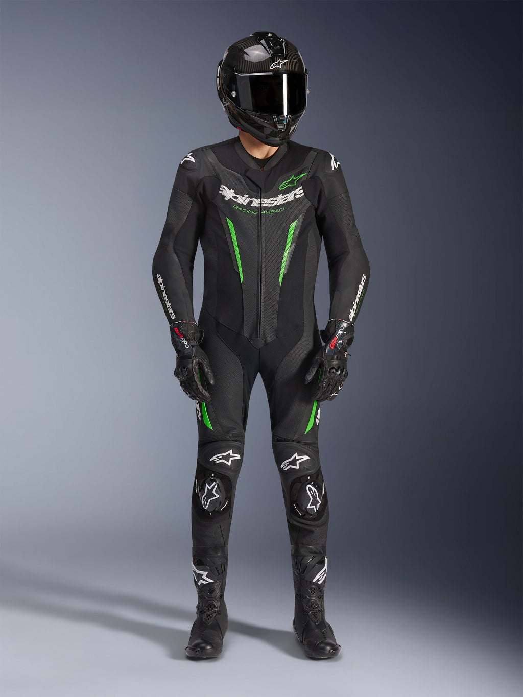 Motorrijder draagt Alpinestars GP Force V2 Leren Pak - 1-delig in zwart en groen, gecombineerd met een carbon fiber helm en racehandschoenen, voorzien van geperforeerde leren panelen en witte Alpinestars-logo's, professionele uitrusting voor circuit en sportief rijden