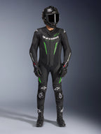 Motorrijder draagt Alpinestars GP Force V2 Leren Pak - 1-delig in zwart en groen, gecombineerd met een carbon fiber helm en racehandschoenen, voorzien van geperforeerde leren panelen en witte Alpinestars-logo's, professionele uitrusting voor circuit en sportief rijden
