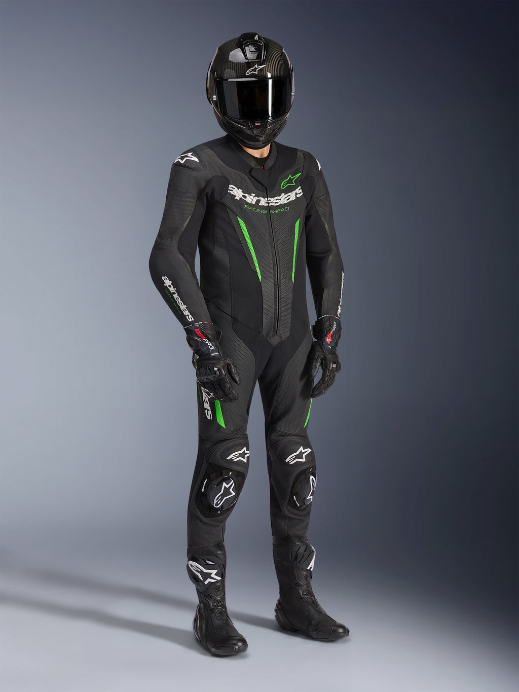 Alpinestars GP Force V2 Leren Pak - 1-delig, zwart en groen, gedragen met bijpassende zwarte helm, racehandschoenen en laarzen, voorzien van felgroene accenten en opvallende witte Alpinestars-branding, professionele circuit- en sportuitrusting