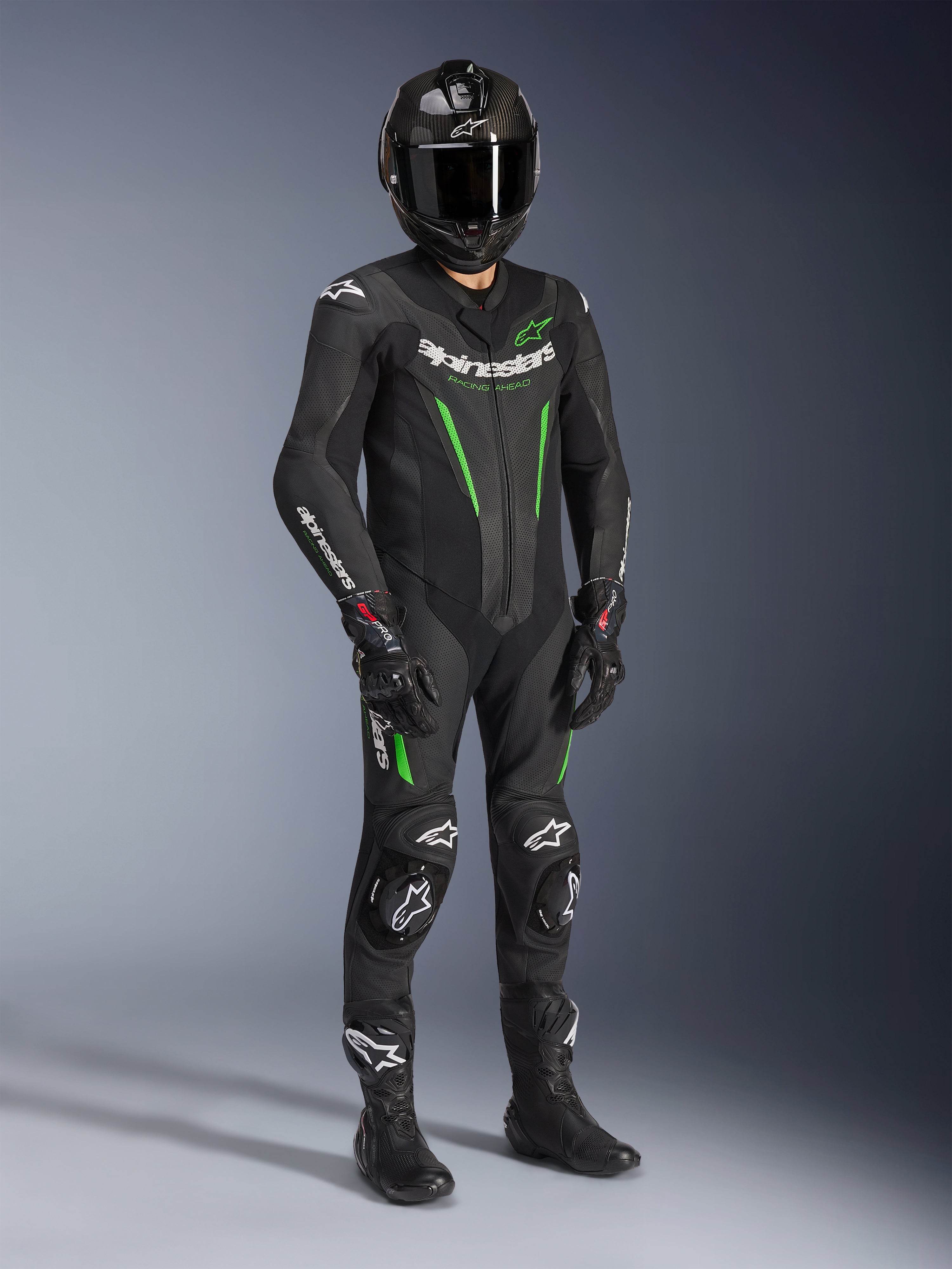 Alpinestars GP Force V2 Leren Pak - 1-delig, zwart en groen, gedragen met bijpassende zwarte helm, racehandschoenen en laarzen, voorzien van felgroene accenten en opvallende witte Alpinestars-branding, professionele circuit- en sportuitrusting
