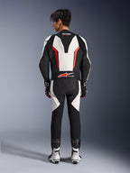 Alpinestars GP Force V2 eendelig leren pak, motorracepak, wit, zwart en fluo rood, achteraanzicht van model dat het pak draagt met racelaarzen en handschoenen, voorzien van een aerodynamische speedhump, accordeon stretchpanelen en Tech-Air Ready branding