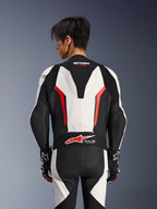 Alpinestars GP Force V2 Leren Pak 1-delig, wit, zwart en fluo rood, achteraanzicht op mannelijk model, met aerodynamische speed hump, geperforeerde leren panelen en Tech-Air Ready-logo op de onderrug, professionele race-uitrusting met zwart-witte handschoenen