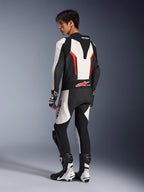 Alpinestars GP Force V2 Leren Pak - 1-delig in wit, zwart en fluorood, achteraanzicht van een motorrijder die de aerodynamische speed hump en geperforeerde leren panelen toont, gecombineerd met bijpassende racelaarzen en handschoenen, ontworpen voor het circuit.