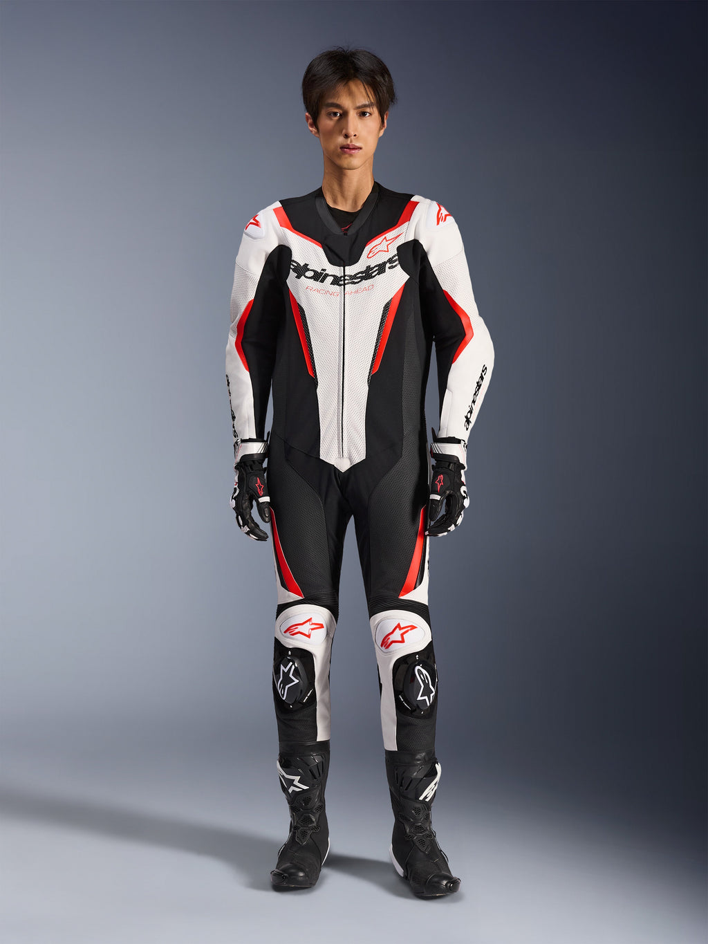 Alpinestars GP Force V2 Leren Pak - 1-delig, Wit Zwart Rood Fluo, eendelig leren motorracepak, vooraanzicht op model, voorzien van geperforeerde panelen en rode accenten, opvallende Alpinestars-branding op de borst, gestyled met professionele racelaarzen en handschoenen