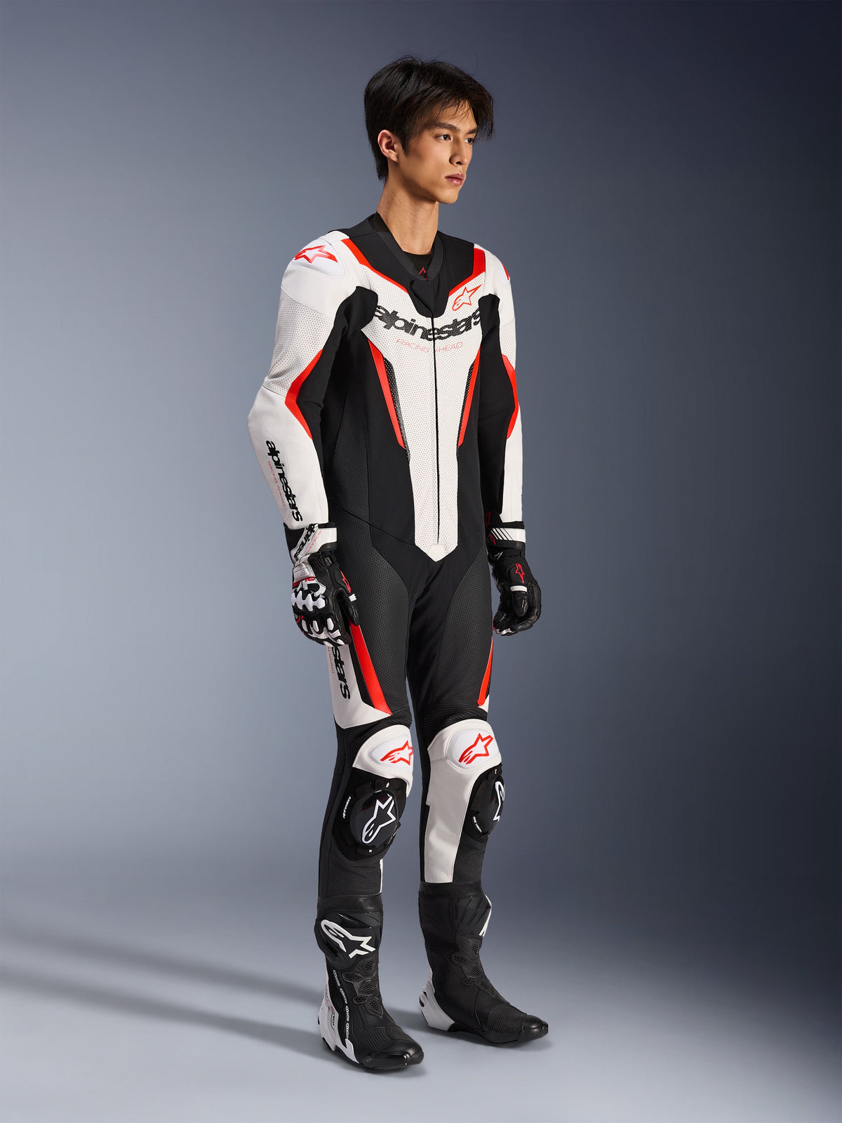 Alpinestars GP Force V2 Leren Pak - 1-delig, eendelig motorracepak, wit, zwart en fluorood, gedragen met bijpassende handschoenen en laarzen, voorzien van geperforeerd leer en opvallende Alpinestars branding, aerodynamisch ontwerp voor prestaties op het circuit