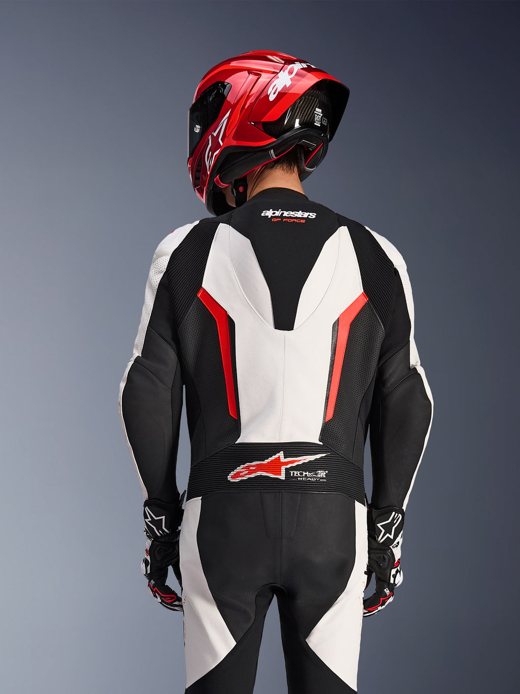 Achteraanzicht van het Alpinestars GP Force V2 1-delig leren pak in White Black Red Fluo, gedragen met een rode racehelm, voorzien van Tech-Air Ready-logo op de onderrug, geperforeerde lederen panelen en accordeon stretchzones voor raceprestaties.