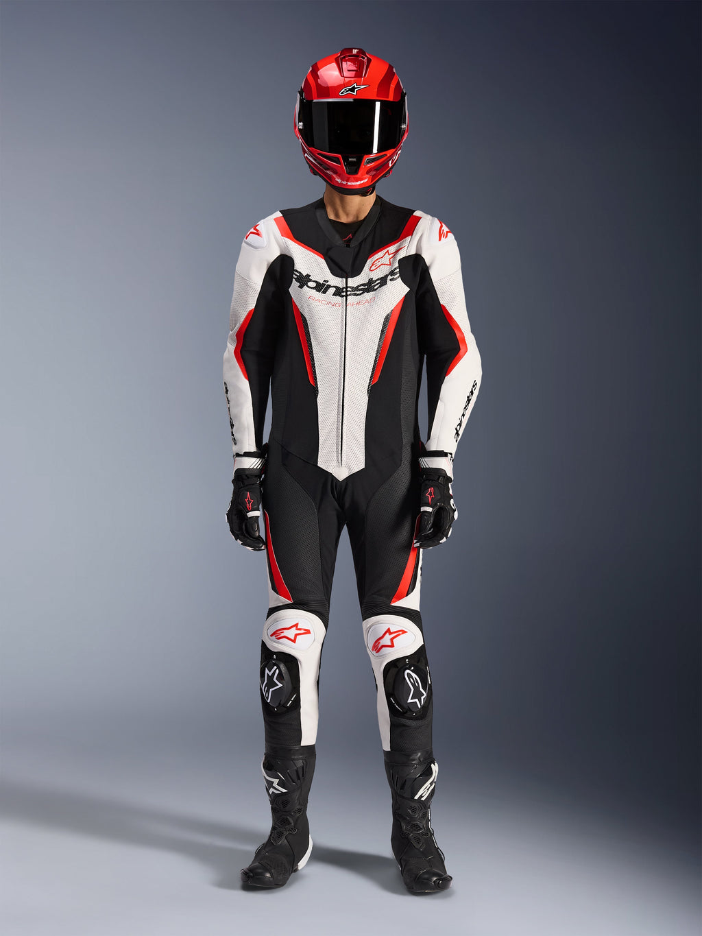 Alpinestars GP Force V2 Leren Pak - 1-delig, wit, zwart en fluo rood, volledige race-uitrusting inclusief rode helm, zwarte handschoenen en laarzen, voorzien van aerodynamisch design en Alpinestars-logo's op de borst en knieën