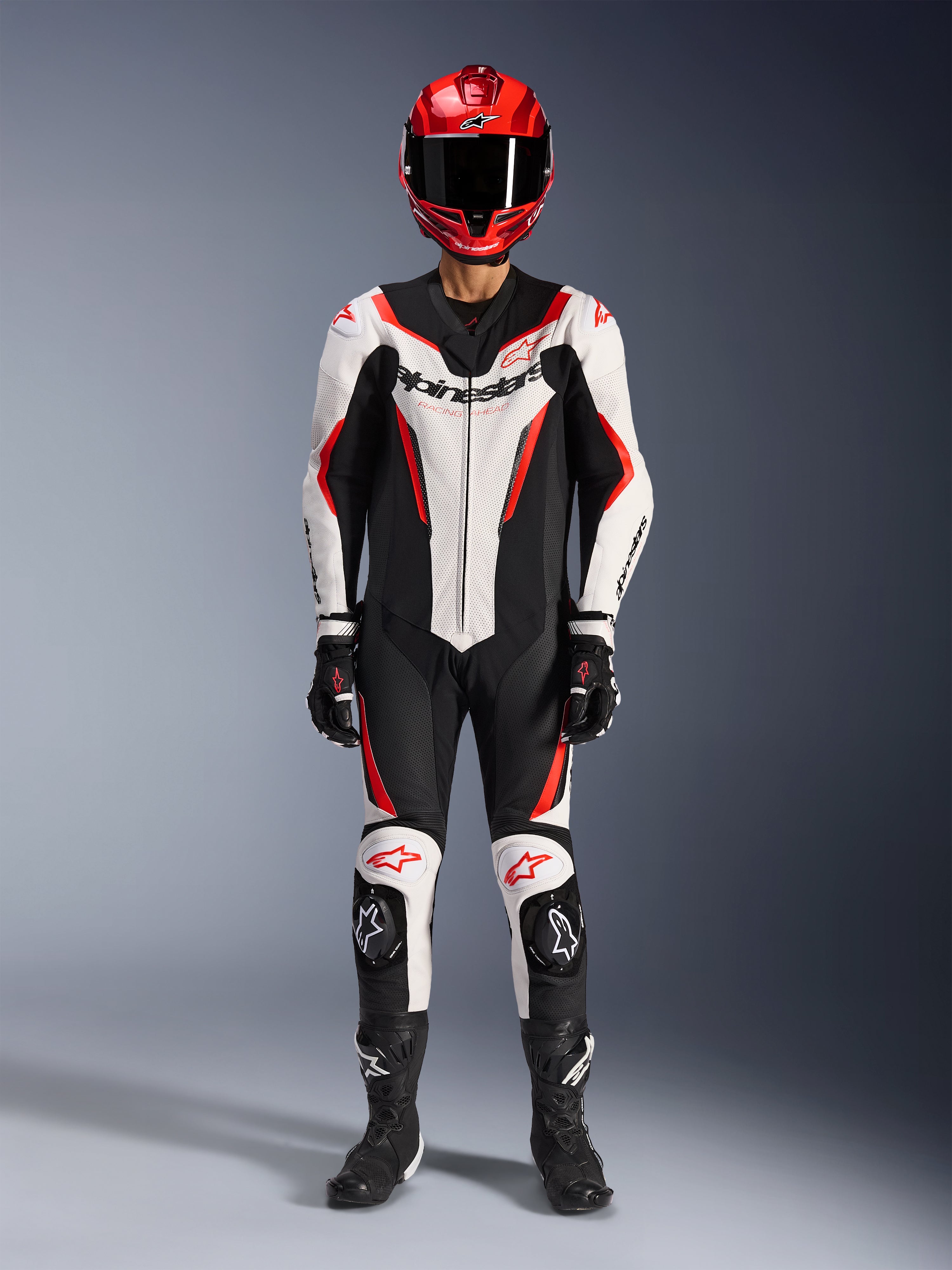 Alpinestars GP Force V2 Leren Pak - 1-delig, wit, zwart en fluo rood, volledige race-uitrusting inclusief rode helm, zwarte handschoenen en laarzen, voorzien van aerodynamisch design en Alpinestars-logo's op de borst en knieën