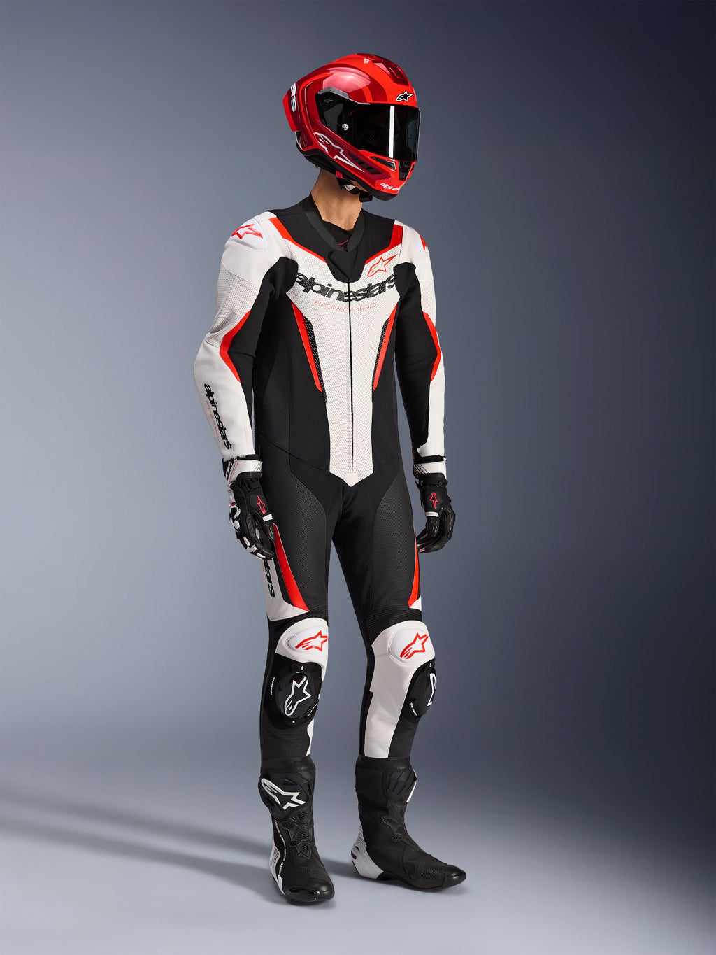 Alpinestars GP Force V2 Leren Pak 1-delig in Wit Zwart en Fluo Rood, studio-opname van een rijder in volledige race-uitrusting inclusief een rode helm, zwarte handschoenen en zwarte laarzen, met een aerodynamische runderleren constructie met opvallende branding en geïntegreerde kniesliders.