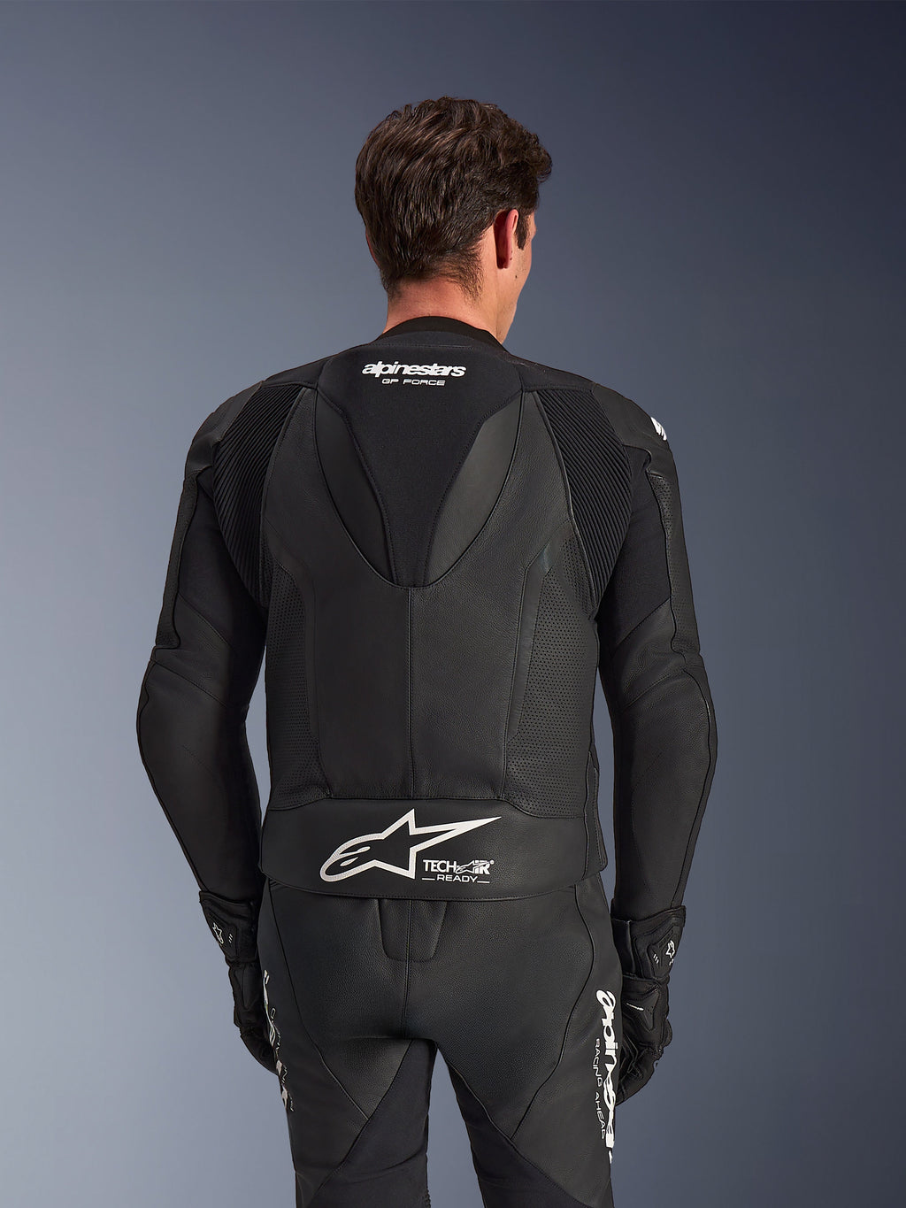 Alpinestars GP Force V2 tweedelig leren pak, zwart, achteraanzicht van de rijder, voorzien van geperforeerde lederen panelen, aerodynamische speedhump met GP Force-branding, wit Alpinestars-logo met Tech-Air Ready-tekst op de onderrug