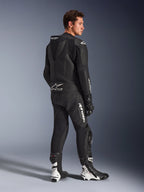 Mannelijk model draagt Alpinestars GP Force V2 2-delig leren motorpak in het zwart met witte logo's, driekwart achteraanzicht met de aerodynamische speedhump en Tech-Air Ready-branding, gecombineerd met zwart-witte racelaarzen en handschoenen, professionele sport- en circuitmotoruitrusting.