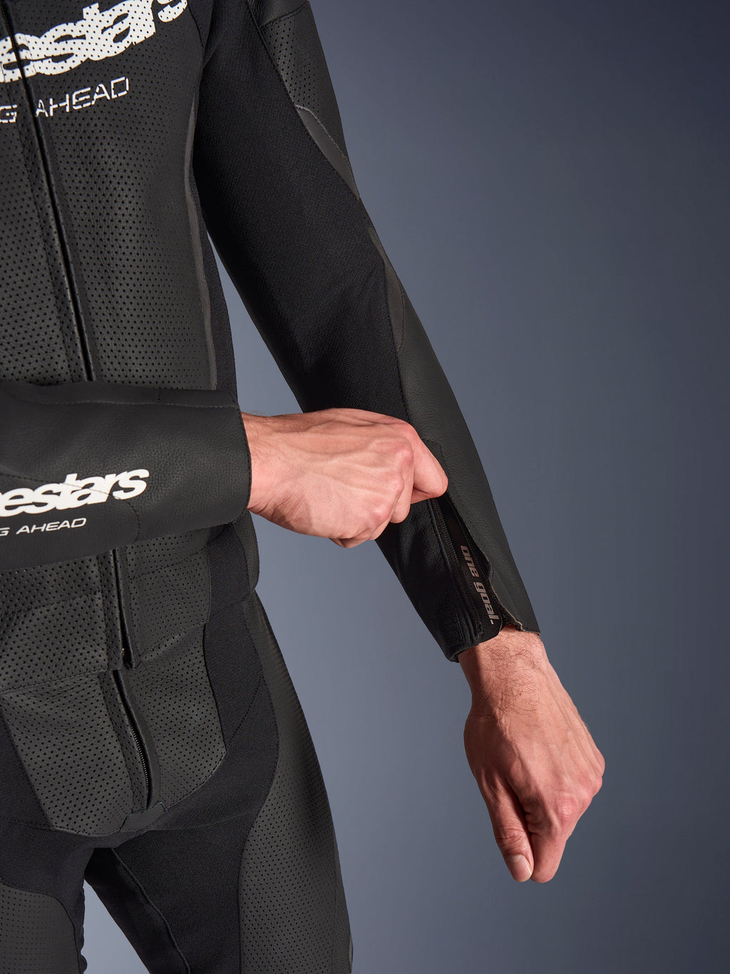 Alpinestars GP Force V2 2-delig leren pak in het zwart, detailopname van de ritsopening aan de onderarm die wordt aangepast, voorzien van geperforeerde leren panelen en stretchstof constructie.
