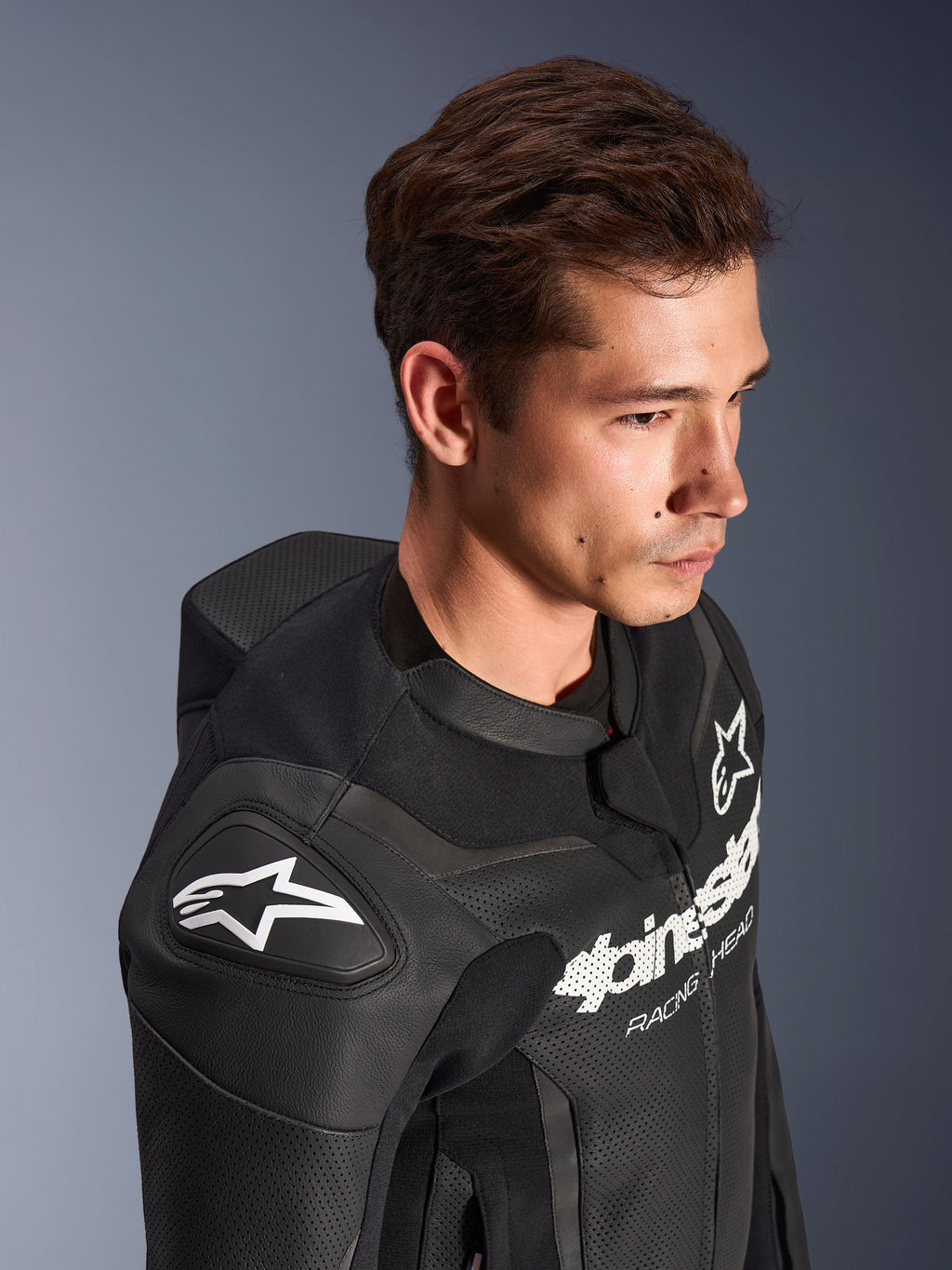Alpinestars GP Force V2 lederen pak, 2-delig, zwart, gedragen door een model, voorzien van de schouder met wit Astar-logo, branding op de borst, geperforeerde lederen panelen en aerodynamische speedhump, hoogwaardige motorrace-uitrusting