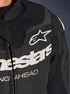Alpinestars GP Force V2 2-delig leren pak, racing/sport motorpak, zwart, close-up van de geperforeerde lederen borst met wit Alpinestars-logo en branding, nadruk op ventilatieopeningen en getextureerde constructie.