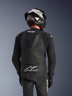Alpinestars GP Force V2 2-delig leren pak, zwart, achteraanzicht van de rijder met aerodynamische speedhump, geperforeerde leren panelen en accordeon-stretchzones op de schouders, Tech-Air Ready-branding op de onderrug, gedragen met bijpassende racehelm en handschoenen.