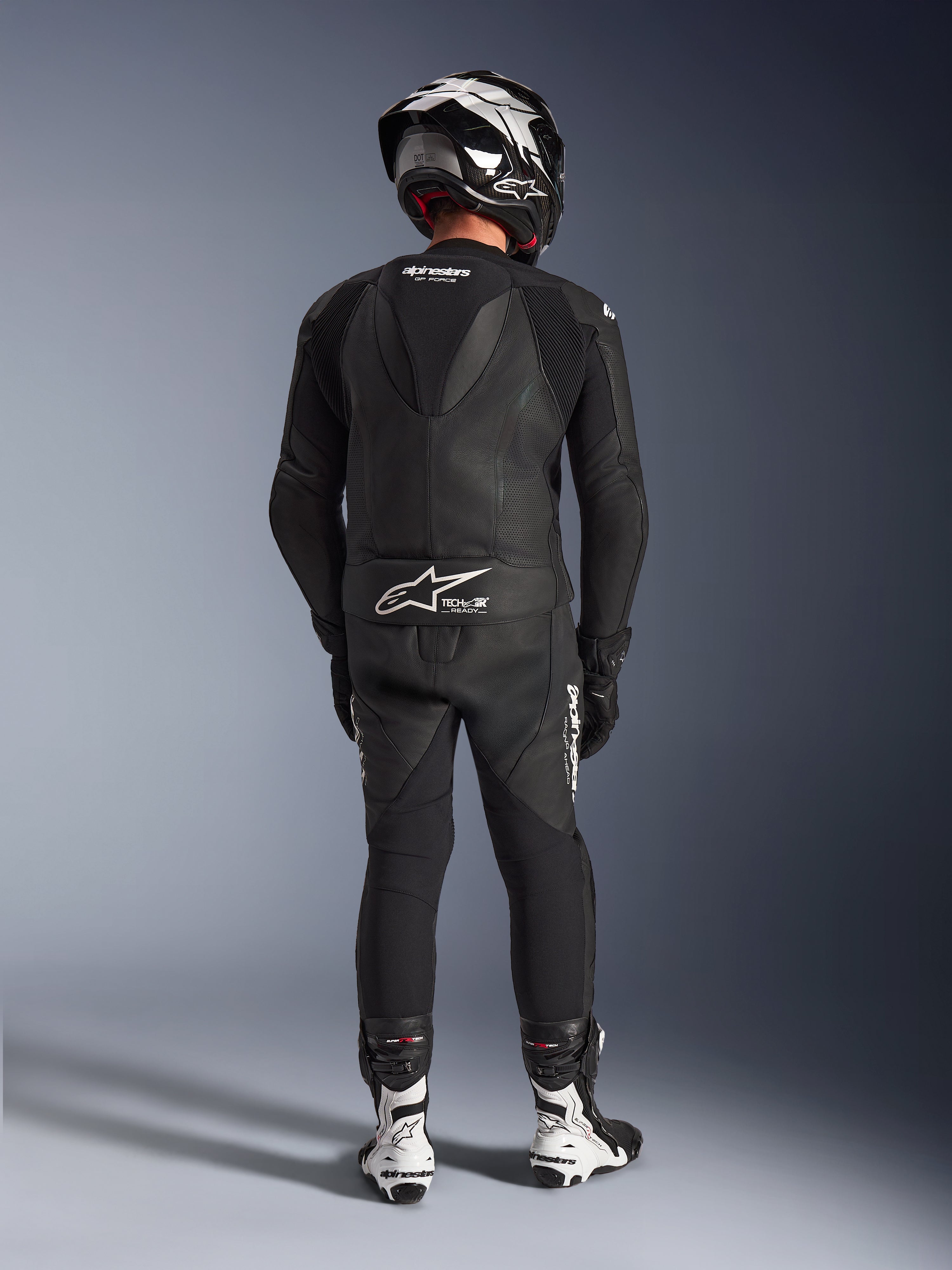 Alpinestars GP Force V2 2-delig leren pak in het zwart, volledig achteraanzicht met aerodynamische speedhump en Tech-Air Ready-branding, gecombineerd met bijpassende zwart-witte helm en witte racelaarzen voor professionele circuitprestaties