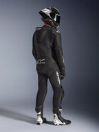 Alpinestars GP Force V2 2-delig leren pak, zwart, achteraanzicht van motorrijder in volledige race-uitrusting, met aerodynamische speedhump, witte logo's en geperforeerd leer, gecombineerd met een carbon helm en zwart-witte racelaarzen