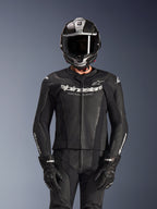 Rijder in Alpinestars GP Force V2 2-delig leren pak in het zwart, geperforeerde leren constructie met wit 'Racing Ahead' logo op de borst, zilveren en carbonfiber integraalhelm, zwarte handschoenen, professionele sport- en circuituitrusting