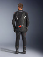Rear view of a rider wearing the Alpinestars GP Force V2 2-Piece Leather Suit, Black with white and red accents, featuring prominent Alpinestars and Tech-Air Ready branding on the back, styled with matching black racing gloves and boots.