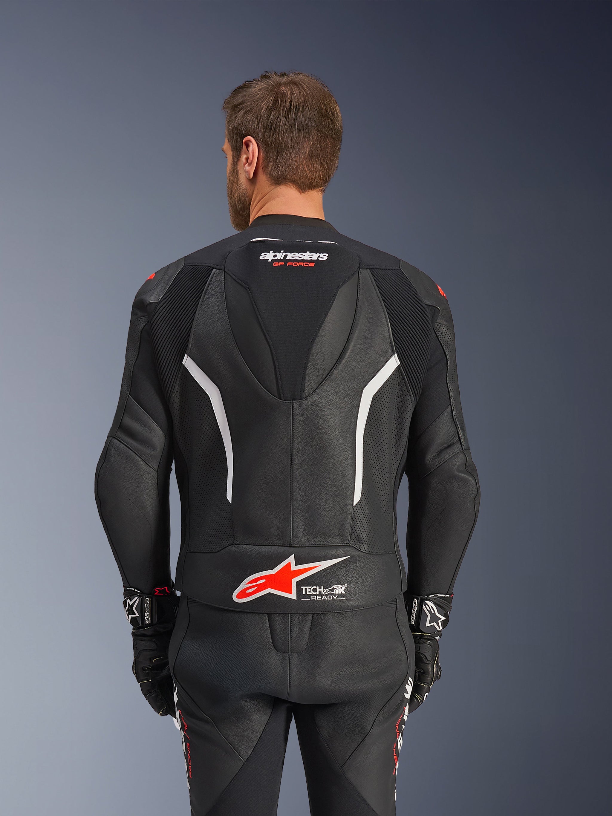 Alpinestars GP Force V2 tweedelig leren pak, zwart, wit en rood fluo, achteraanzicht van het leren jack, voorzien van het Tech-Air Ready logo, witte accenten, geperforeerde lederen panelen en accordeonstretch voor bewegingsvrijheid.