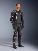 Alpinestars GP Force V2 tweedelig leren pak, zwart, wit en fluo rood, gedragen door een model met zwarte racelaarzen en handschoenen, voorzien van geperforeerde lederen panelen, witte aerodynamische accenten en fluo rode logo's op schouders en knieën, professionele motorrace-uitrusting