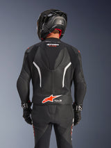 Achteraanzicht van het Alpinestars GP Force V2 2-delig leren pak in het zwart, voorzien van geperforeerd leer, witte accenten en rode Alpinestars-branding op de onderrug, gedragen met een zwarte motorhelm en racehandschoenen.
