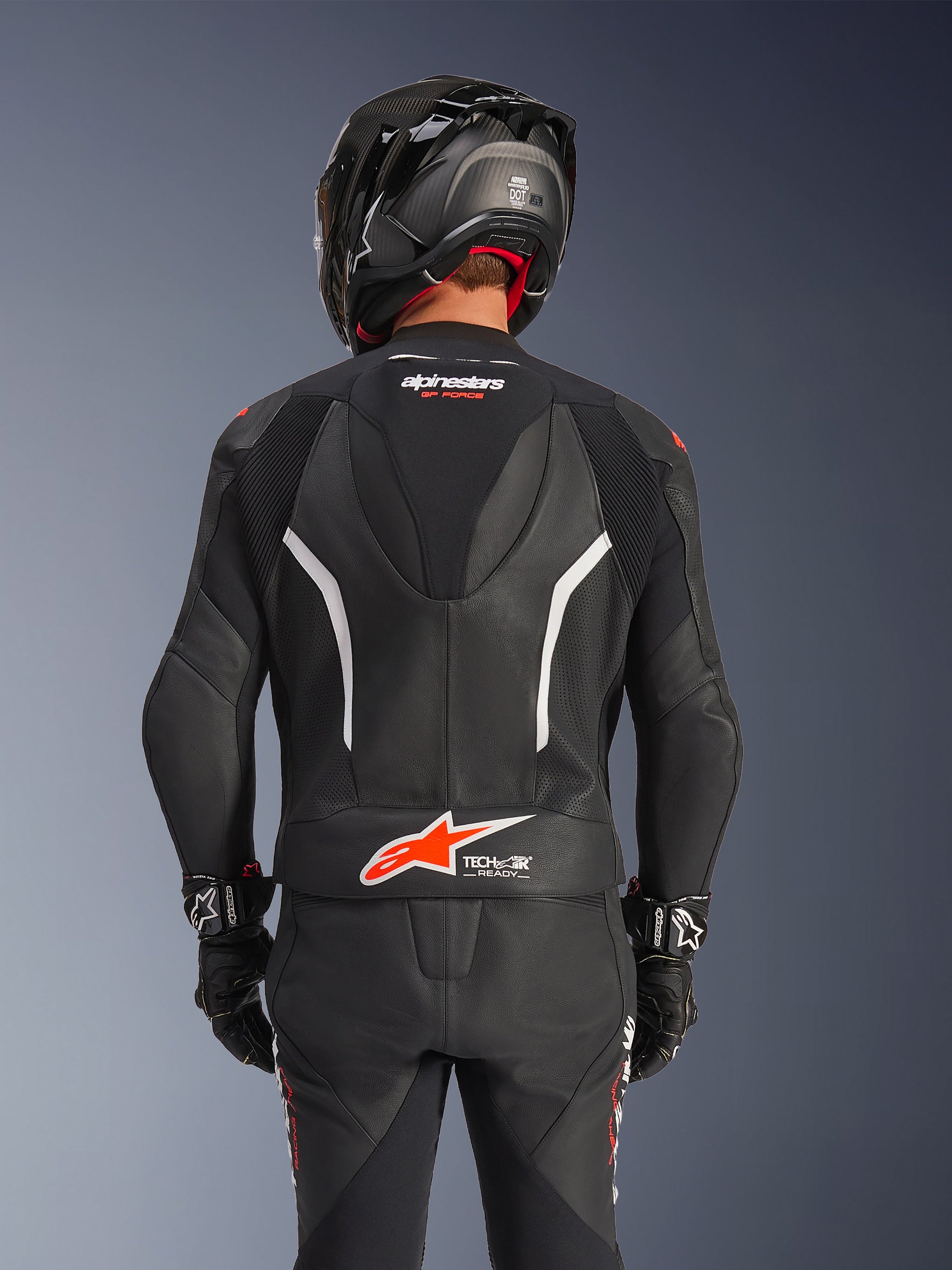 Achteraanzicht van het Alpinestars GP Force V2 2-delig leren pak in het zwart, voorzien van geperforeerd leer, witte accenten en rode Alpinestars-branding op de onderrug, gedragen met een zwarte motorhelm en racehandschoenen.