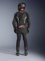 Motorrijder van achteren gezien in het Alpinestars GP Force V2 tweedelig leren pak, zwart met witte en rood fluo accenten, voorzien van een aerodynamische hump en Tech-Air Ready-logo, compleet met zwarte racehelm, handschoenen en laarzen.