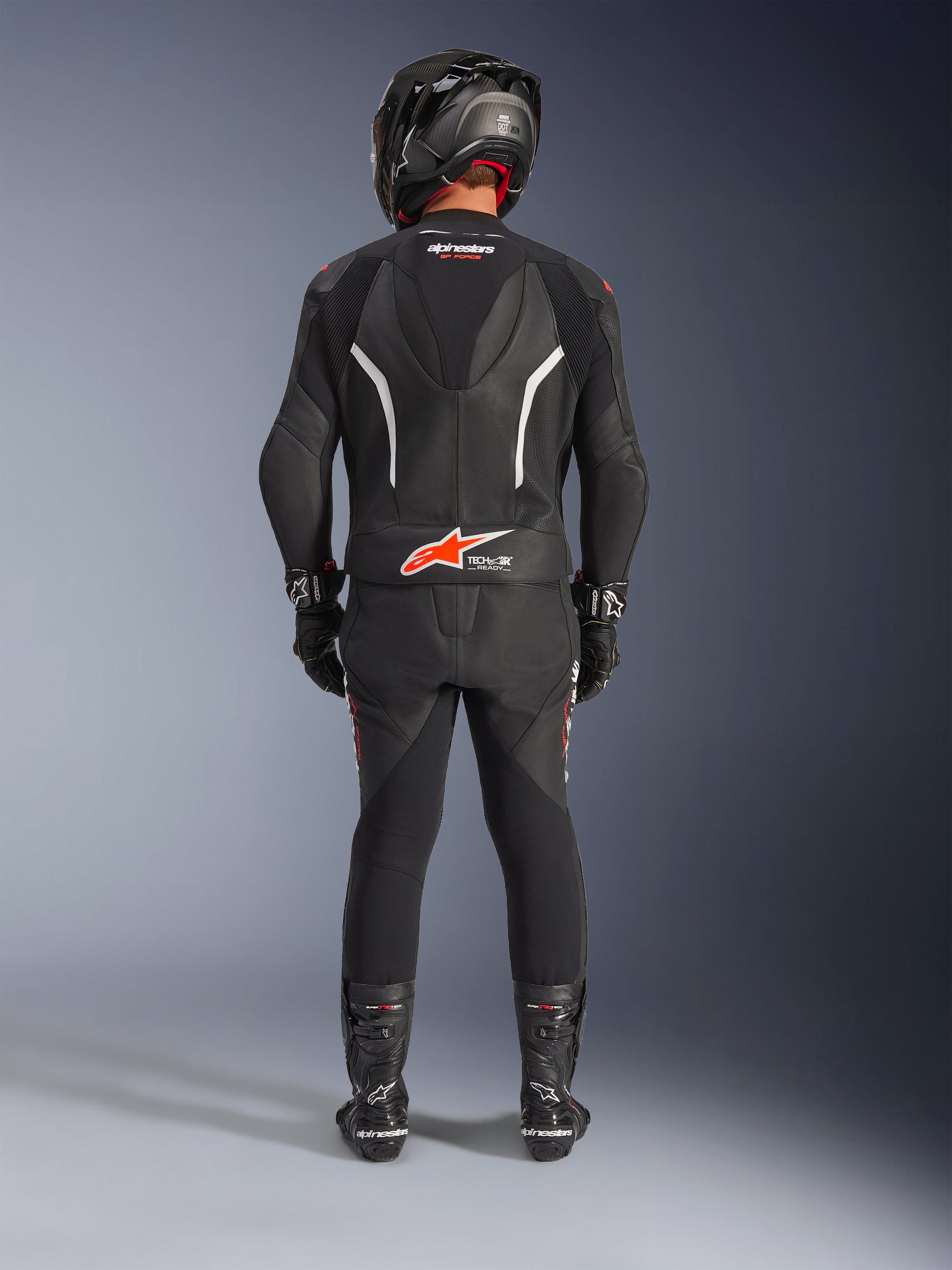 Motorrijder van achteren gezien in het Alpinestars GP Force V2 tweedelig leren pak, zwart met witte en rood fluo accenten, voorzien van een aerodynamische hump en Tech-Air Ready-logo, compleet met zwarte racehelm, handschoenen en laarzen.