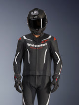 Alpinestars GP Force V2 tweedelig leren pak, zwart wit en fluo rood, gedragen door een rijder met een carbon integraalhelm en zwarte racehandschoenen, voorzien van geperforeerde leren panelen en Alpinestars-branding op de borst.