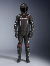 Alpinestars GP Force V2 tweedelig leren pak, motorracepak, zwart wit en rood fluo, voorzien van wit Alpinestars-logo op de borst en rode accenten op de schouders en knieën, gedragen met zwarte integraalhelm, zwarte handschoenen en zwarte laarzen voor een complete performance-uitrusting