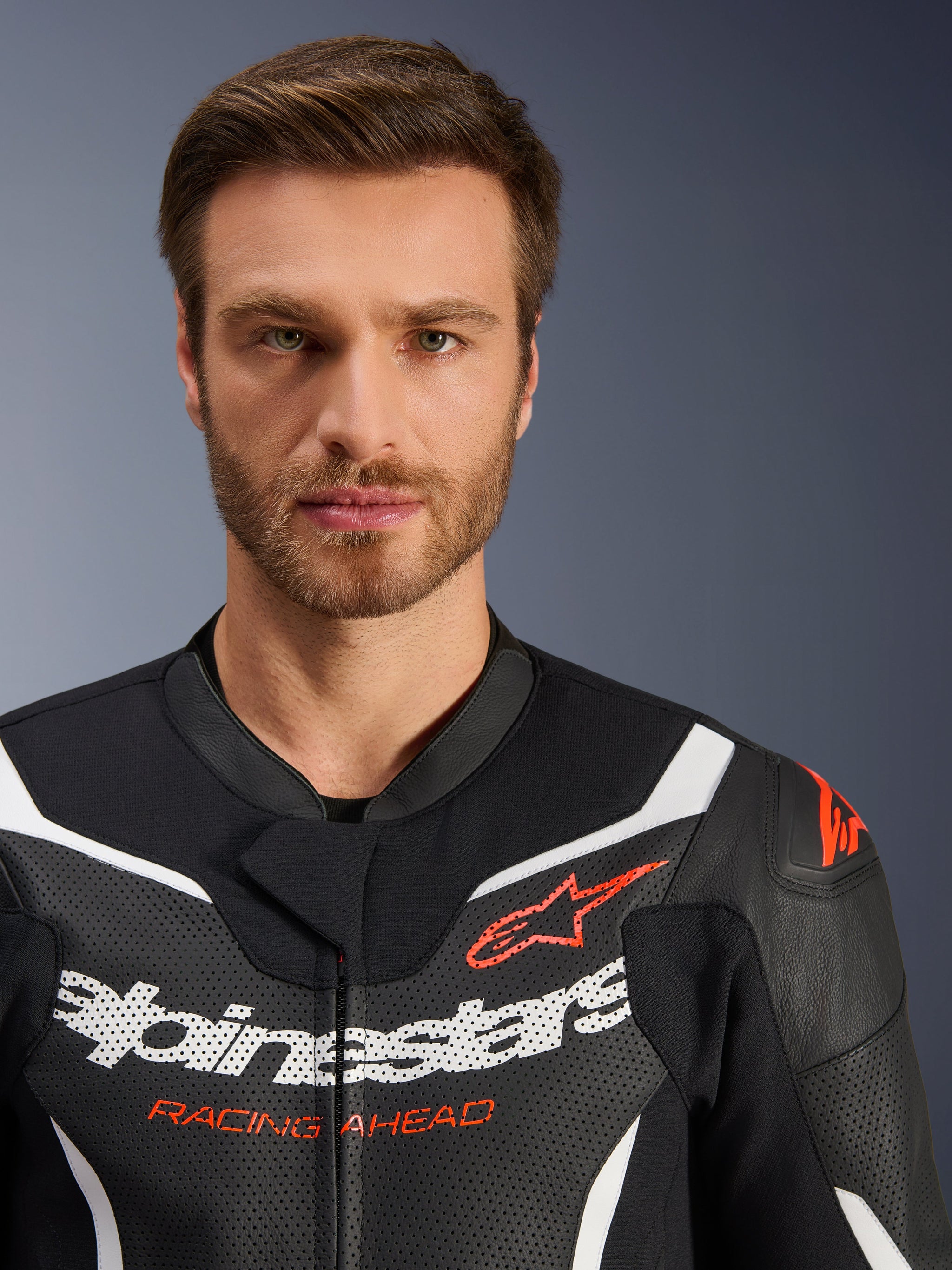 Alpinestars GP Force V2 tweedelige leren motorpak jas, zwart wit fluo rood, close-up portret met geperforeerd leer, witte Alpinestars-branding en rode 'RACING AHEAD'-tekst, hoogwaardige motoruitrusting