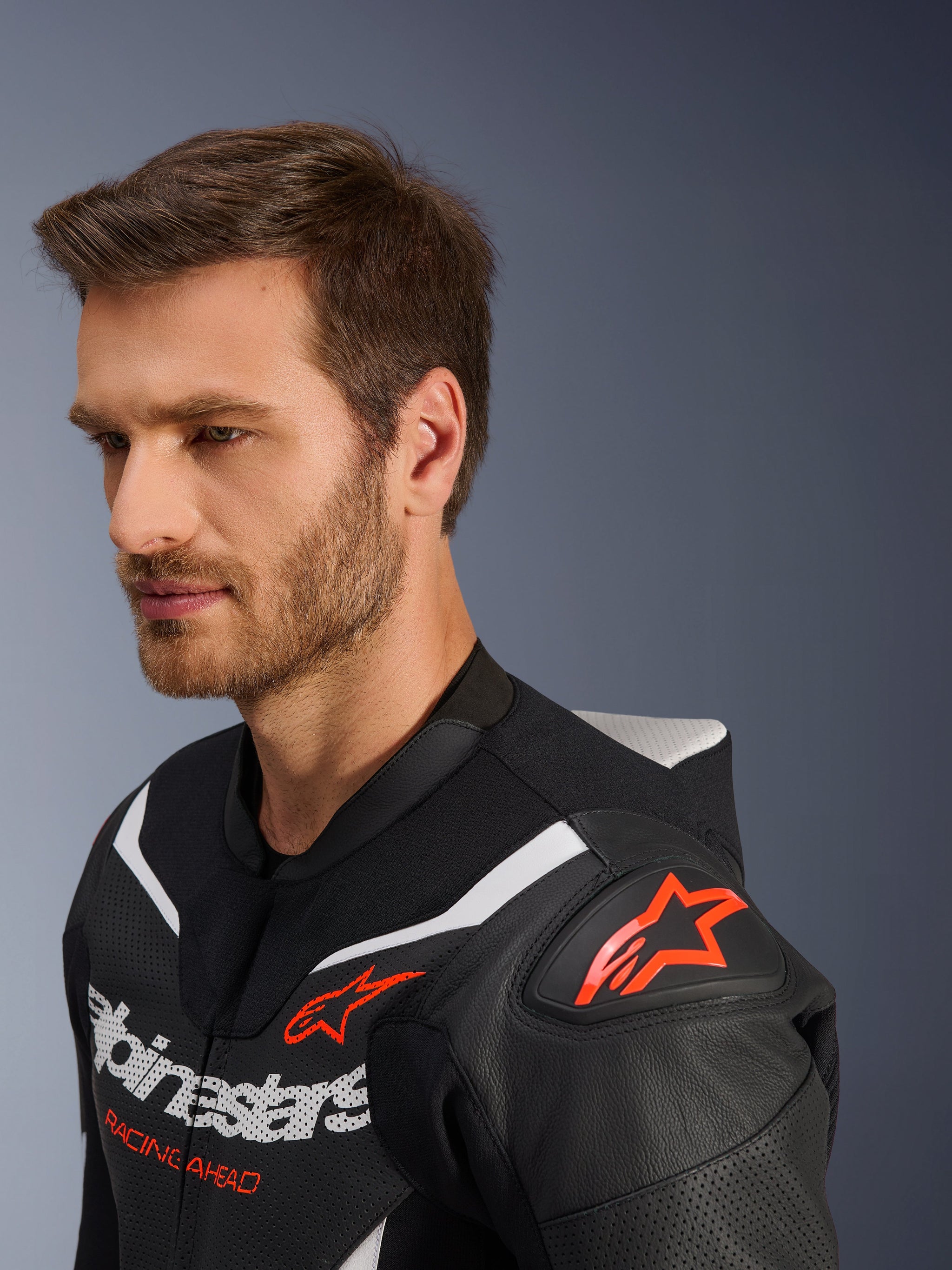 Alpinestars GP Force V2 tweedelig leren pak, close-up van de jas gedragen door een mannelijk model, zwart, wit en fluo rood, voorzien van geperforeerd leer, rood sterlogo op de schouder, aerodynamische speed hump en Alpinestars-branding op de borst, professionele motorracekleding