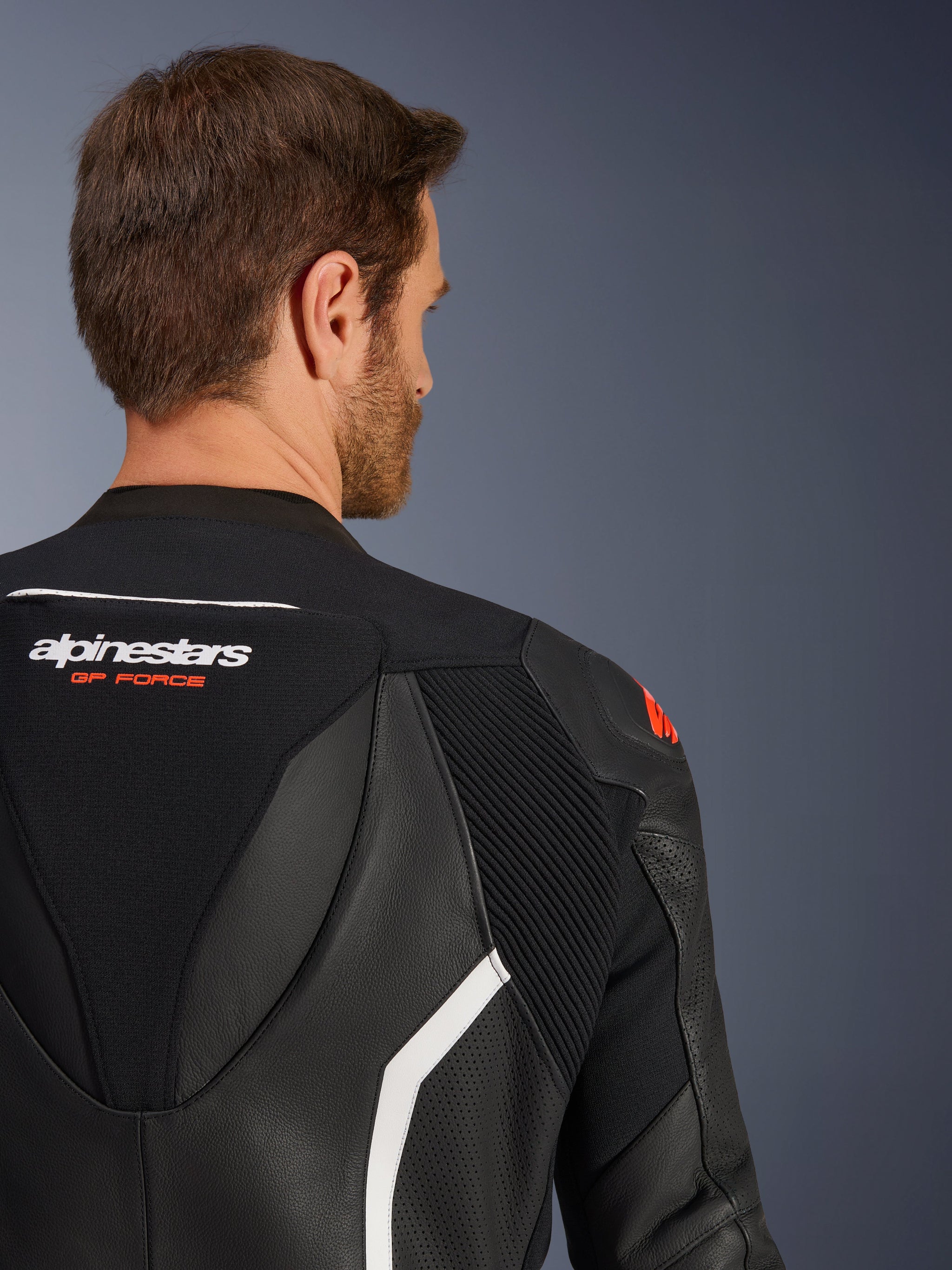 Alpinestars GP Force V2 tweedelig leren pak, close-up van de bovenrug en schouder op een mannelijk model, zwart leer met witte en rode accenten, Alpinestars GP Force-branding, met geperforeerde panelen en accordeon-stretchzones voor motorracen