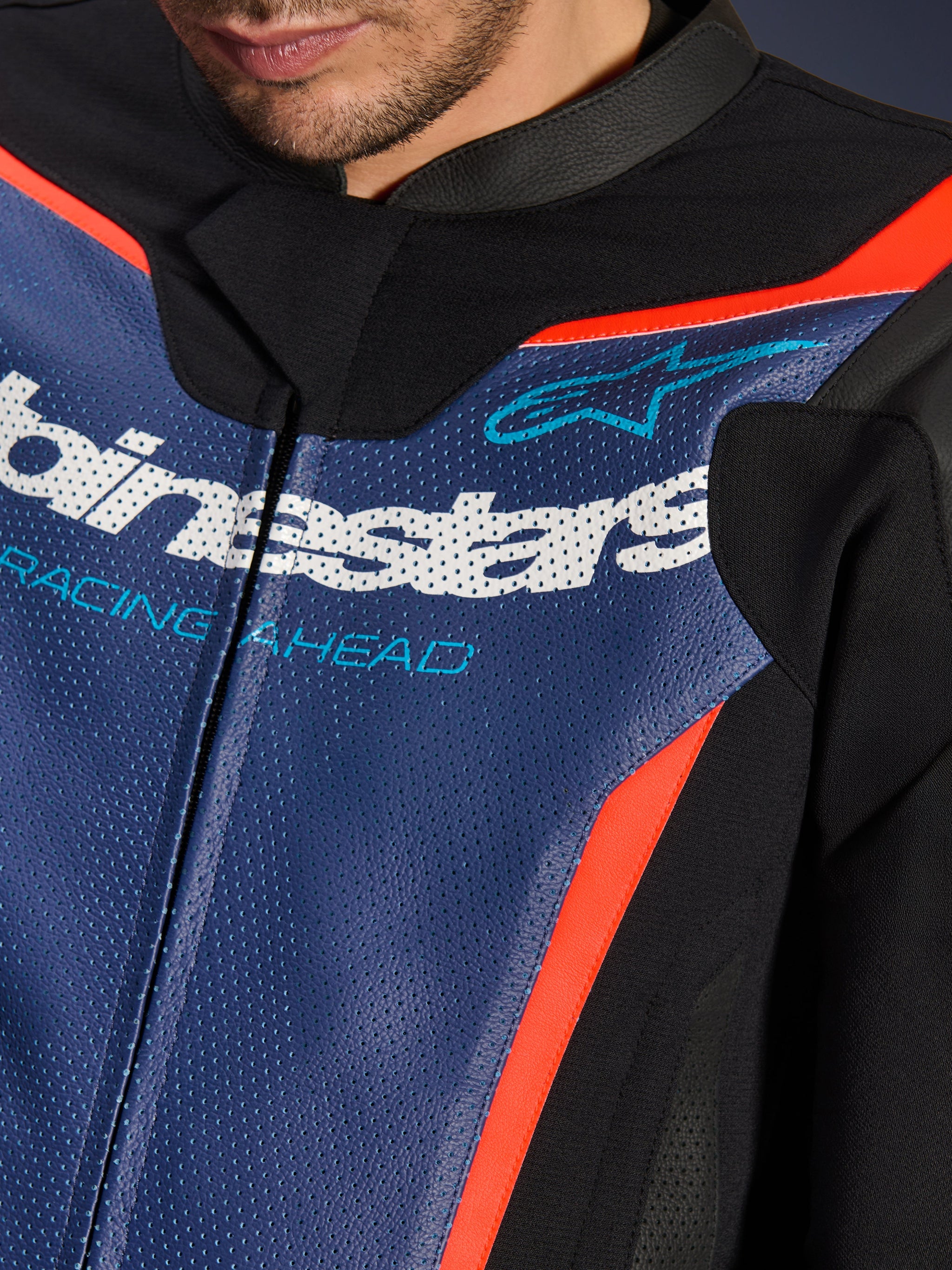 Alpinestars GP Force V2 Leren Pak, 2-delig, detailopname van de borst, geperforeerd blauw leer met wit logo en 'RACING AHEAD' tekst, fluo rode accenten en zwarte panelen, professionele sportuitrusting voor motorrijders