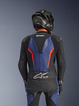 Alpinestars GP Force V2 2-delig lederen pak, zwart blauw rood fluo, achteraanzicht met aerodynamische speedhump en Tech-Air Ready-branding, premium runderleer met stretchzones, gedragen met een zwarte carbon fiber helm, professionele motorrace-uitrusting