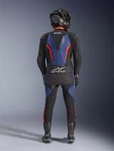 Alpinestars GP Force V2 Leren Pak 2-delig, zwart blauw rood fluo, volledig achteraanzicht van een rijder in complete race-uitrusting, met blauwe lederen panelen op de rug en benen met fluorescerende rode accenten, Tech-Air® Ready-logo op de onderrug, gecombineerd met een carbon helm, zwarte handschoenen en racelaarzen.