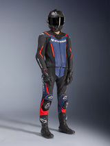 Alpinestars GP Force V2 lederen pak - 2-delig, zwart met blauw en fluo rood, gedragen met een carbon helm, zwarte racehandschoenen en laarzen, voorzien van geperforeerde lederen panelen en wit Alpinestars-logo, professionele sportieve rijuitrusting