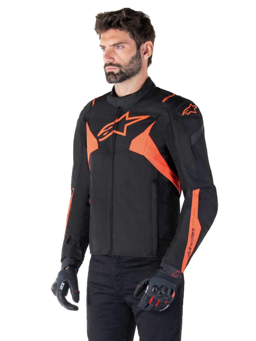 Alpinestars T-Jaws V4 Waterproof Jacket, zwart en fluo rood, sportieve motorjas gedragen door een mannelijk model, voorzien van prominente oranje ster-logo's op de borst en schouders, gecombineerd met zwarte handschoenen en broek