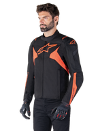 Alpinestars T-Jaws V4 Waterproof Jacket, zwart en fluo rood, sportieve motorjas gedragen door een mannelijk model, voorzien van prominente oranje ster-logo's op de borst en schouders, gecombineerd met zwarte handschoenen en broek