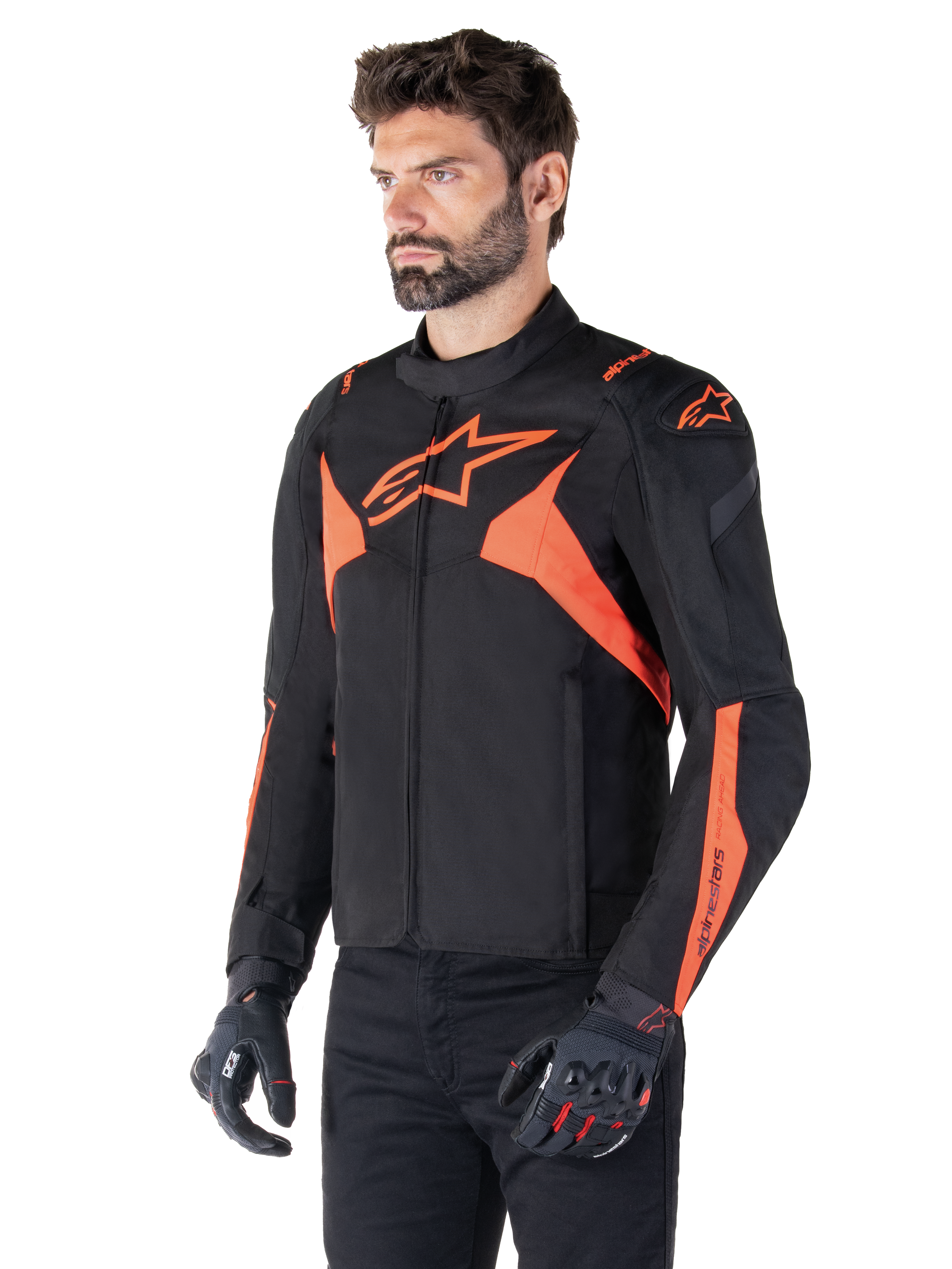 Alpinestars T-Jaws V4 Waterproof Jacket, zwart en fluo rood, sportieve motorjas gedragen door een mannelijk model, voorzien van prominente oranje ster-logo's op de borst en schouders, gecombineerd met zwarte handschoenen en broek