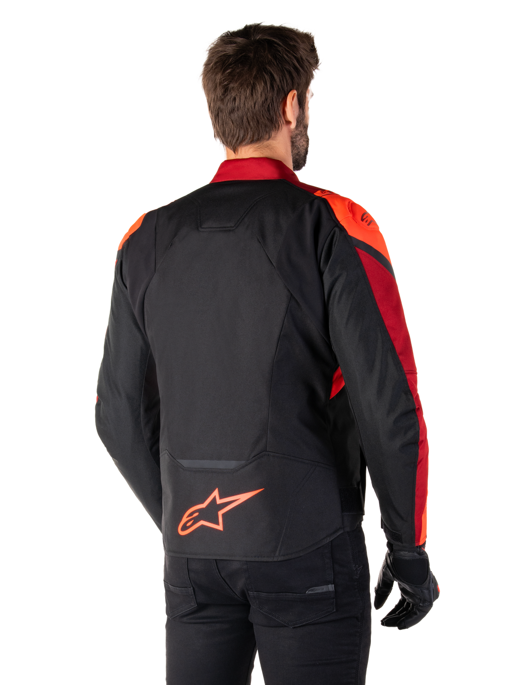 Achteraanzicht van een man die de Alpinestars T-Jaws V4 Waterproof Jas draagt in Black Red Fluo Dark Red, met opvallende rode accenten op de schouders en mouwen, een fluo rood Alpinestars-logo op de onderrug, gecombineerd met een zwarte broek en handschoenen.